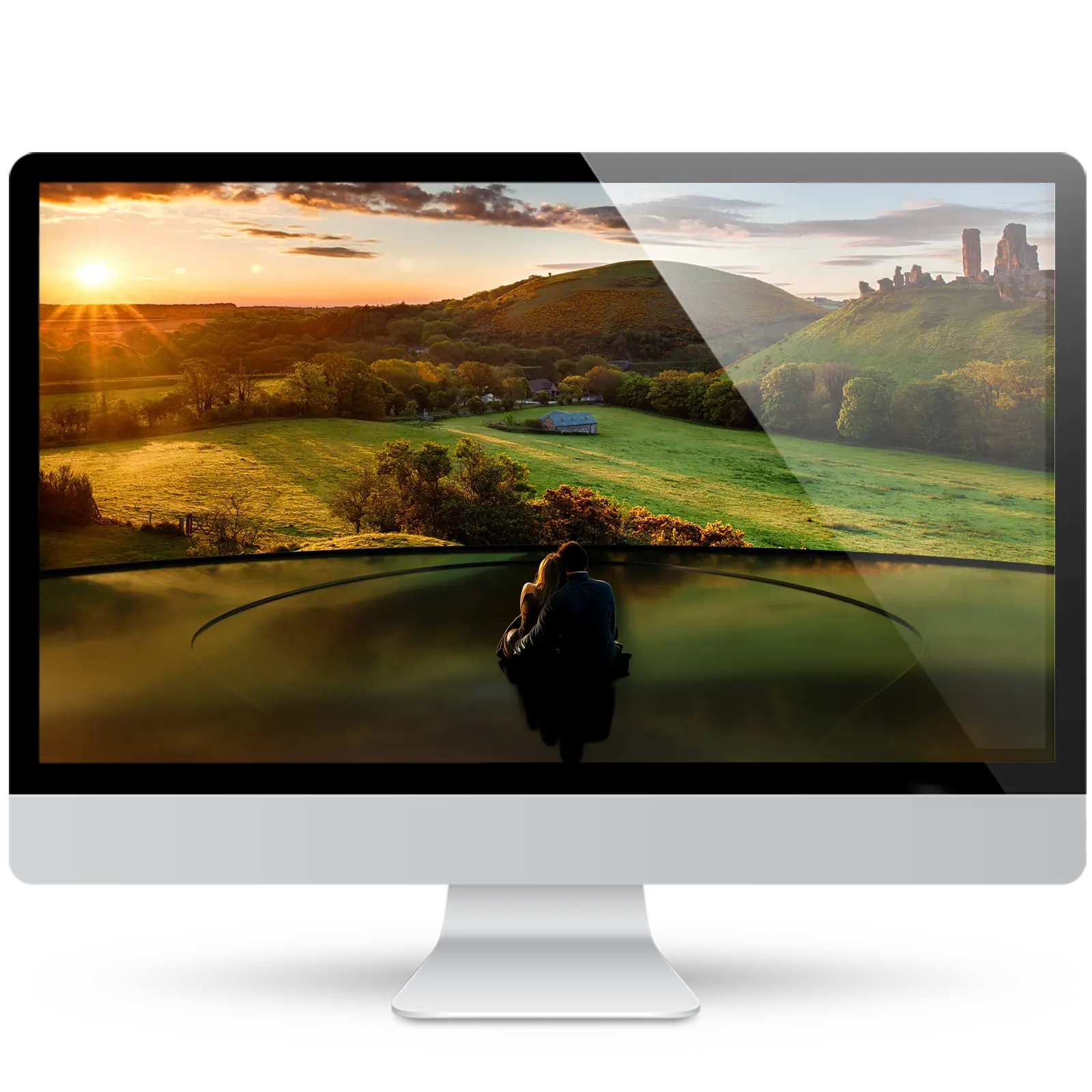 Desktop monitor showing a romantic wallpaper: a couple embracing on a glossy stage, looking out over green countryside hills and castle ruins at sunset.