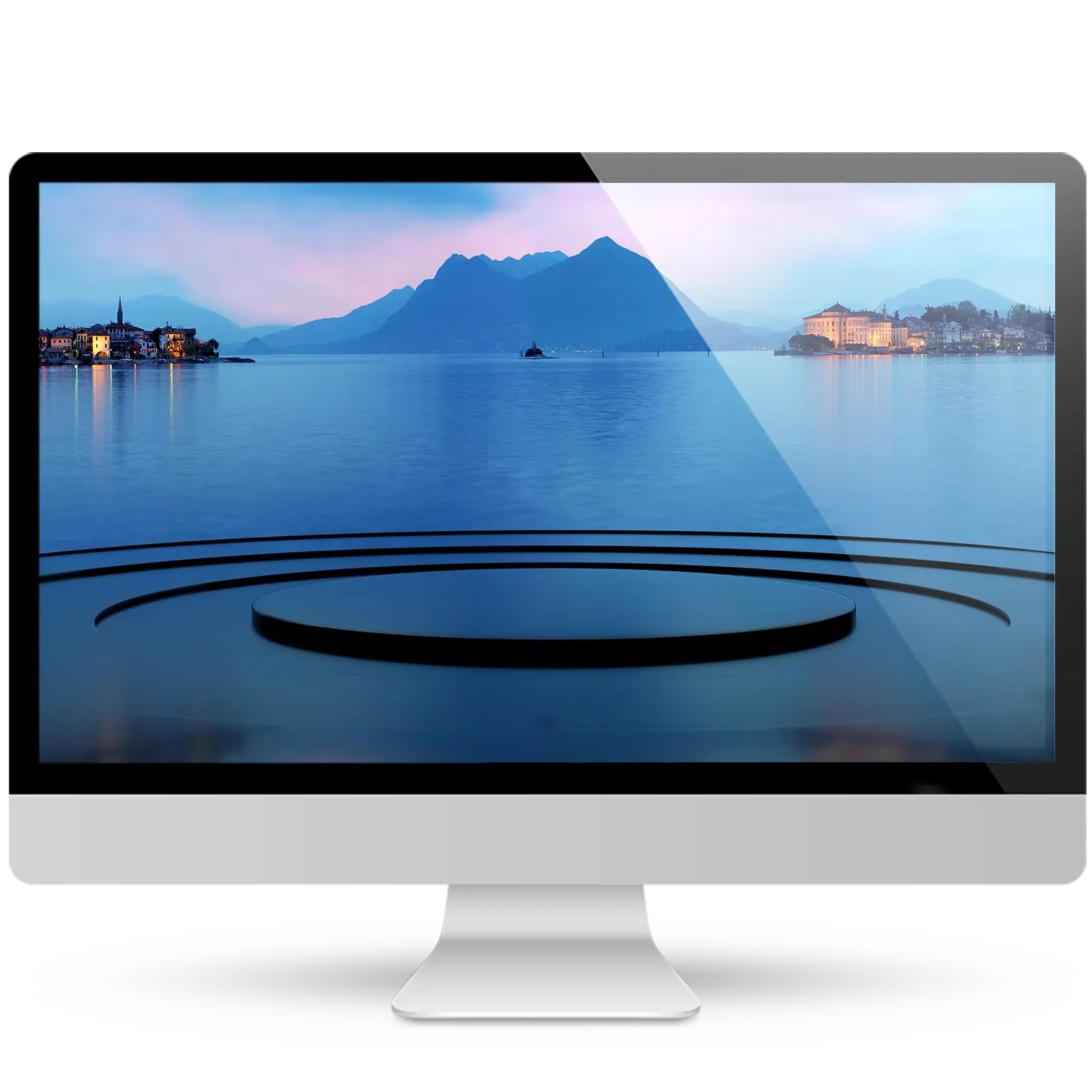 Desktop monitor showing a wallpaper of a calm blue lake at dusk, with lit lakeside villages and misty mountains, above a glossy round stage.