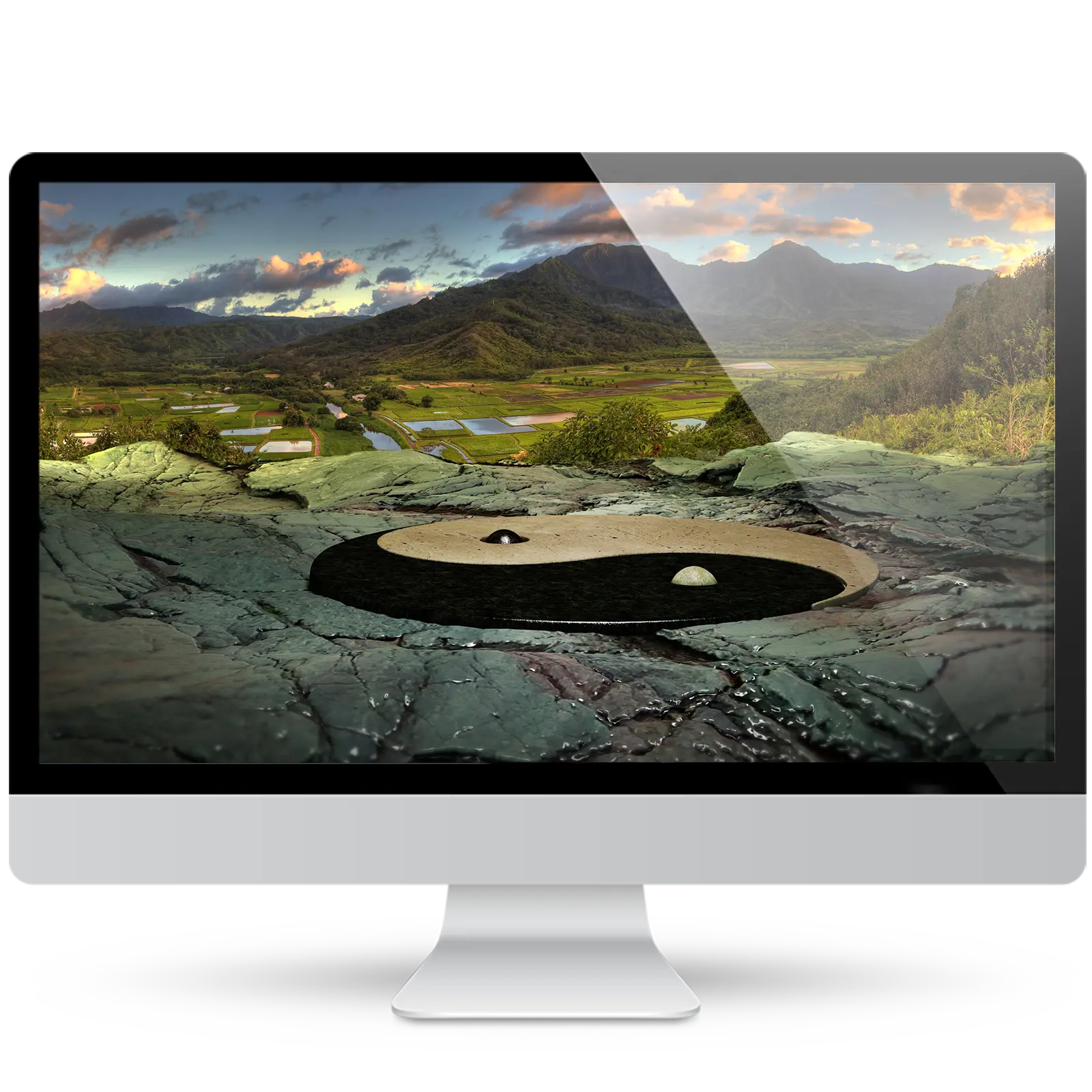 Desktop monitor showing a zen wallpaper: a stone yin-yang symbol set into wet rock, overlooking a green valley of taro fields and mountains at sunset.